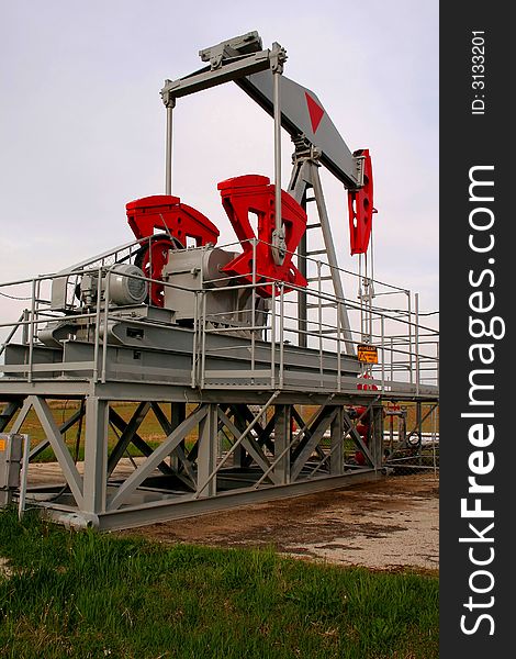Grey and red oil pump on a green field. Grey and red oil pump on a green field.