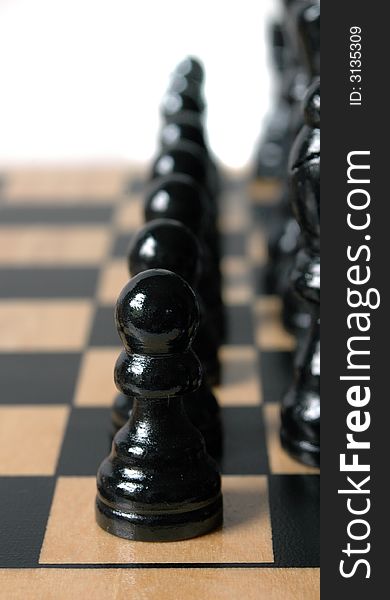 This is a row of black pawns set up in a chess game on a wooden board. This is a row of black pawns set up in a chess game on a wooden board.