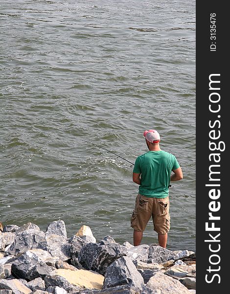 A man on the rocky bank of a river fishing. A man on the rocky bank of a river fishing