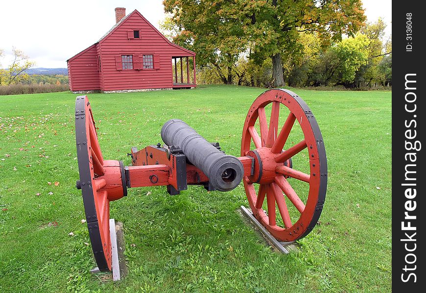 A Red cannon situated in front of a red wooden house.