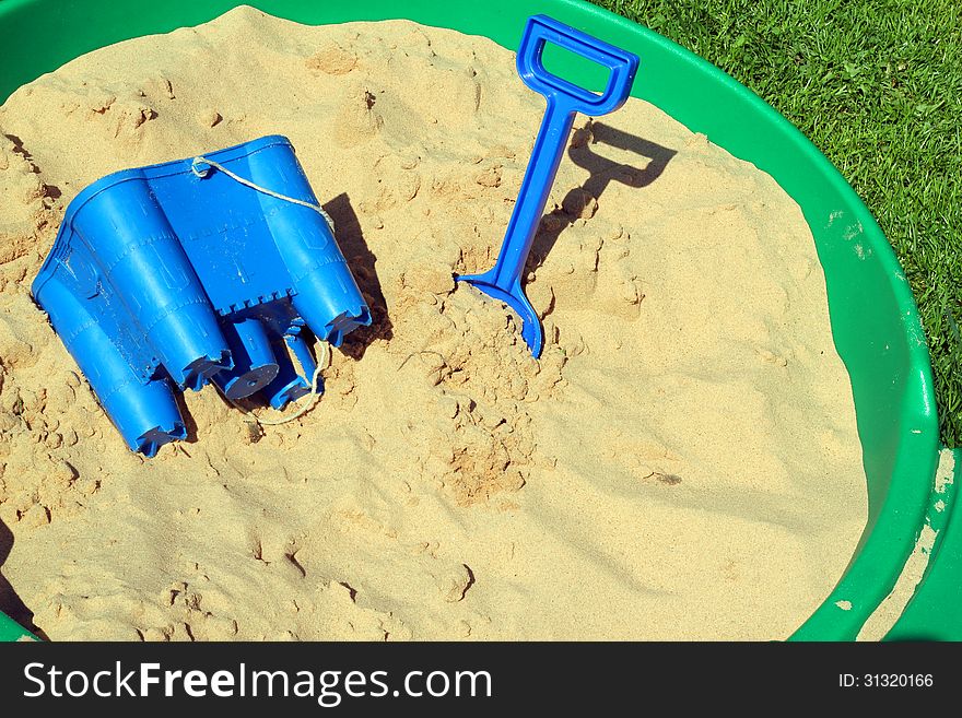 A childs sand pit with a bucket and spade in a garden on the grass. A childs sand pit with a bucket and spade in a garden on the grass.