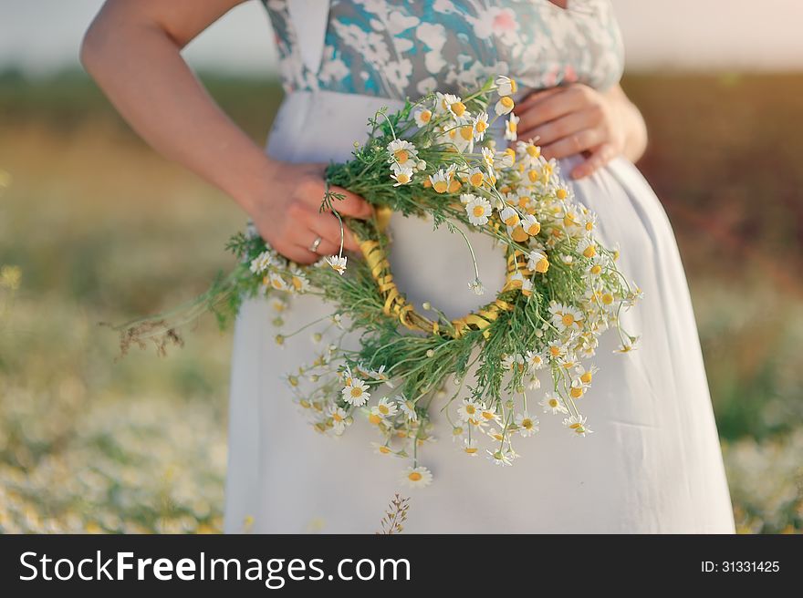 Against the background of the field of chamomile belly of a pregnant woman with a wreath of daisies in her hand. Against the background of the field of chamomile belly of a pregnant woman with a wreath of daisies in her hand
