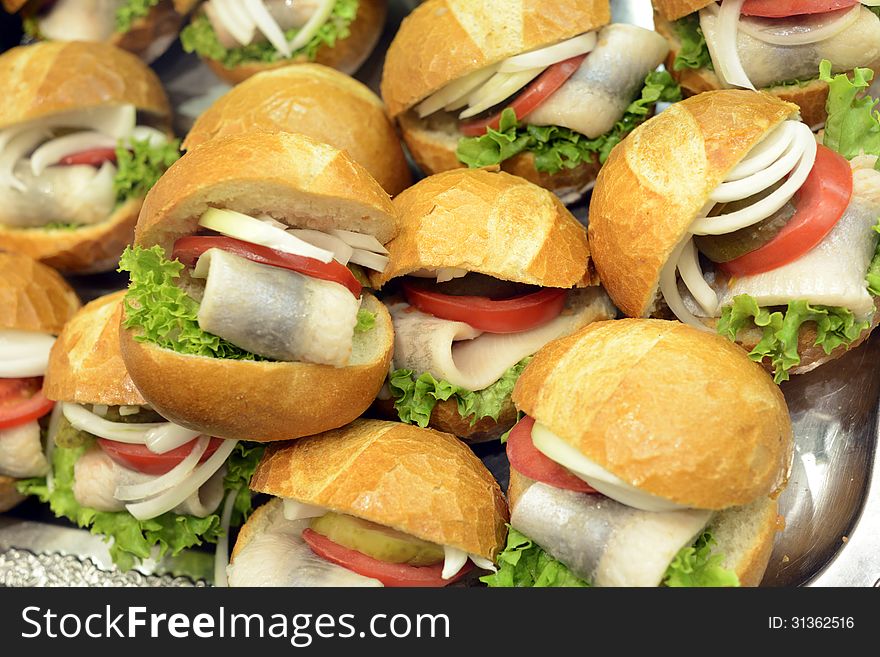 Closeup image of fresh and delicious seafood rolls stacked. The bread is filled with fresh raw fish and decorated with green salad, onions and tomatos. Closeup image of fresh and delicious seafood rolls stacked. The bread is filled with fresh raw fish and decorated with green salad, onions and tomatos.