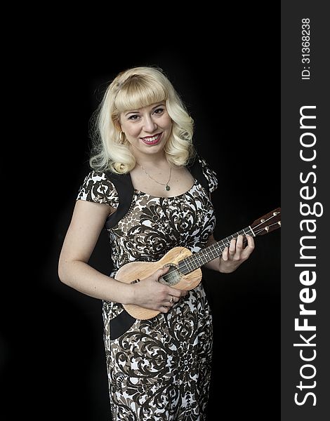 Portrait of a beautiful young woman with blond hair and brown eyes shot on a black background and playing a ukulele. Portrait of a beautiful young woman with blond hair and brown eyes shot on a black background and playing a ukulele.