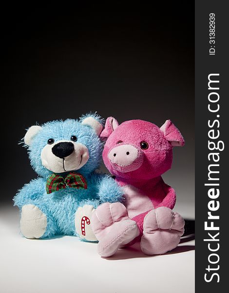 A blue bear and pink pig toy smile and stare off into the distance. A blue bear and pink pig toy smile and stare off into the distance.