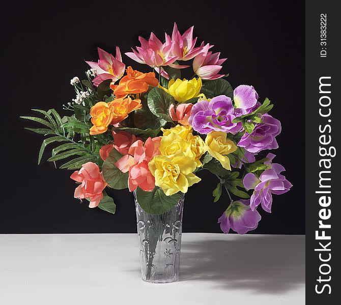 A Bouquet of Fake Flowers against a black background and on a white table. A Bouquet of Fake Flowers against a black background and on a white table.