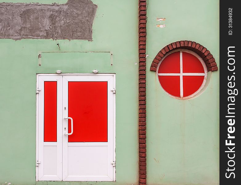 Red round window and a red door on a green old wall with bricks. Red round window and a red door on a green old wall with bricks