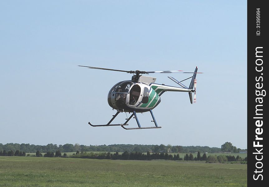 Small two-place civilian helicopter flying low over the ground above a grassy field. Small two-place civilian helicopter flying low over the ground above a grassy field.