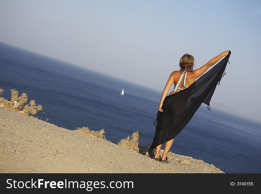 Young woman holding a cloth against the wind on the egde to the sea. Young woman holding a cloth against the wind on the egde to the sea