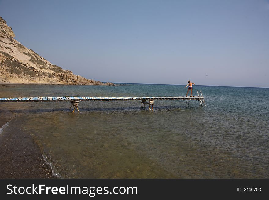 A young boy is standing on a plank and throws rocks into the sea. A young boy is standing on a plank and throws rocks into the sea