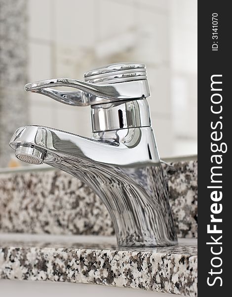 A stainless steel bathroom faucet with foaming nozzle on peppered marble. A stainless steel bathroom faucet with foaming nozzle on peppered marble