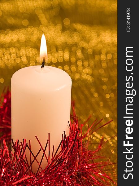Burning candle with red tinsel in a shimmering golden background. Burning candle with red tinsel in a shimmering golden background