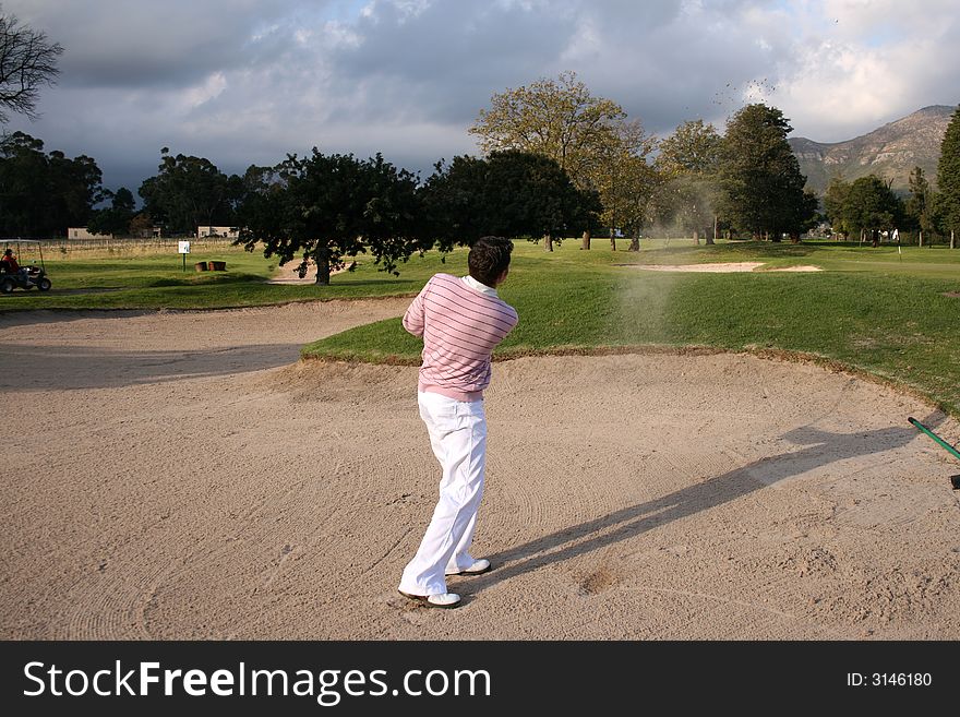 Young golfer hitting a bunker shot, the sand still in the air