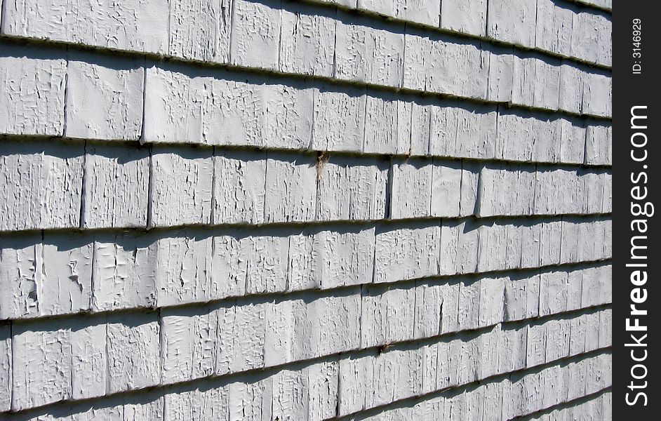 A weathered surface of painted shingles on an old building, with a slightly slanted view for interest. A weathered surface of painted shingles on an old building, with a slightly slanted view for interest