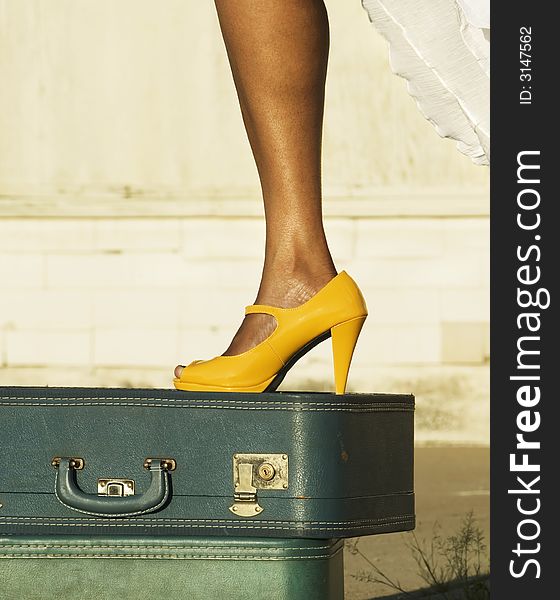 African American woman's leg and foot in a yellow shoe atop a couple suitcases. African American woman's leg and foot in a yellow shoe atop a couple suitcases.