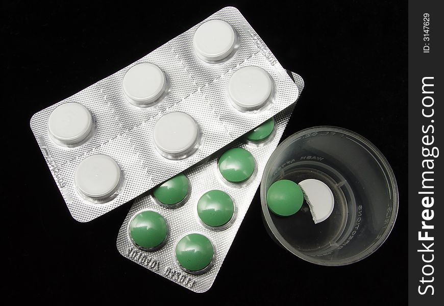 Green and white pills with glass on the blck background. Green and white pills with glass on the blck background