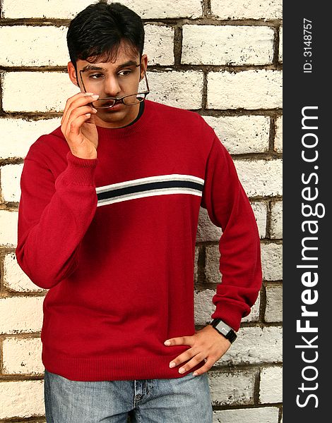 Fashion shoot of young indian man posing with brick background while taking off his glasses. Fashion shoot of young indian man posing with brick background while taking off his glasses