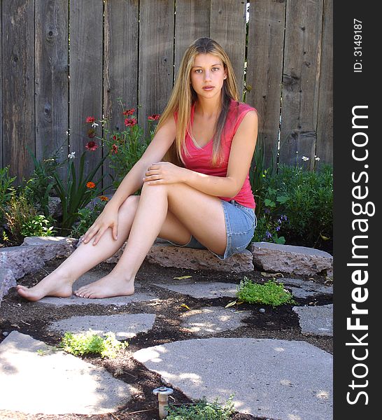 Teenage girl sitting on the ledge of flower garden. Teenage girl sitting on the ledge of flower garden