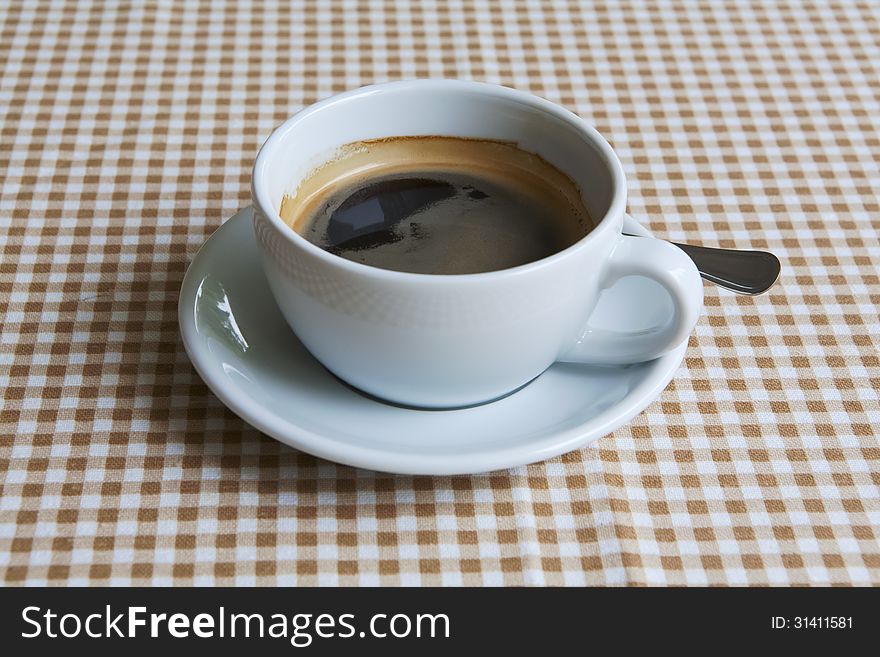 Cup of black coffee on table dressed with tablecloth