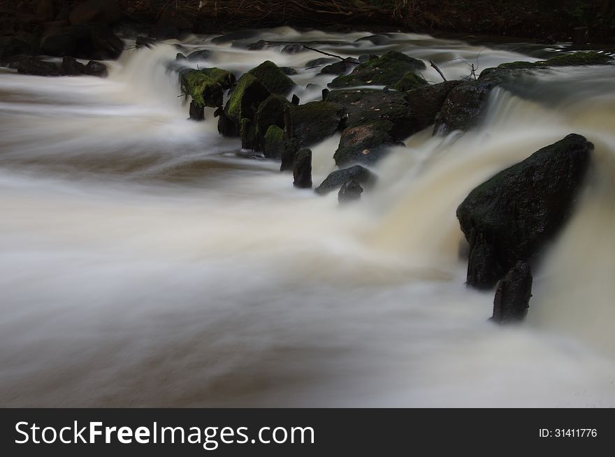 The photograph shows foamy waterfall on a small river. Due to the long exposure time of the effect of freezing water was obtained. The photograph shows foamy waterfall on a small river. Due to the long exposure time of the effect of freezing water was obtained.