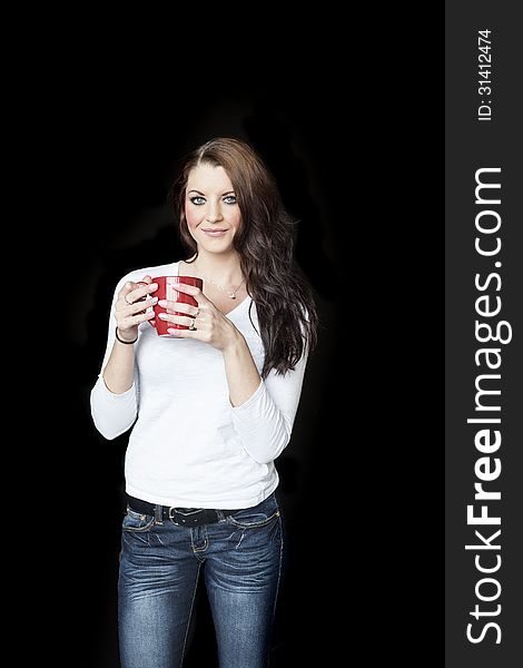 Portrait of a beautiful young woman with brown hair and blue eyes. She is on a black background and drinking coffee from a red cup. Portrait of a beautiful young woman with brown hair and blue eyes. She is on a black background and drinking coffee from a red cup.