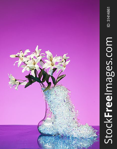 A bouquet of white flowers in a vase with silver decorative tinsel against a bright pink background. A bouquet of white flowers in a vase with silver decorative tinsel against a bright pink background.