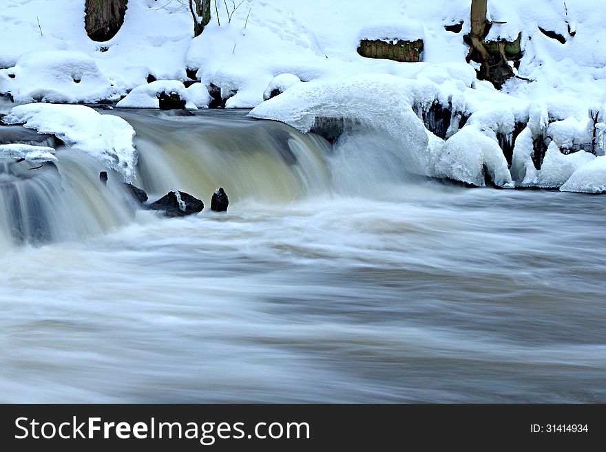 The photograph shows a small waterfall in the winter. The bank is snow on the surface of the water formed ice caps. Due to the long exposure time of the effect of freezing water was obtained. The photograph shows a small waterfall in the winter. The bank is snow on the surface of the water formed ice caps. Due to the long exposure time of the effect of freezing water was obtained.