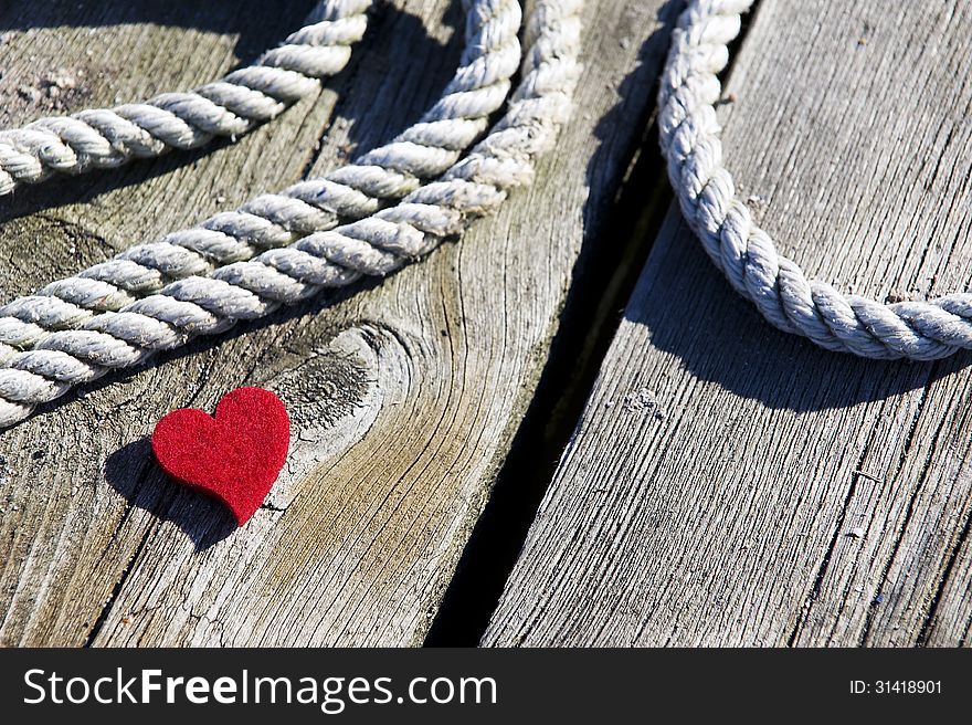 Red heart on worn wooden bridge, rope in the background. Red heart on worn wooden bridge, rope in the background