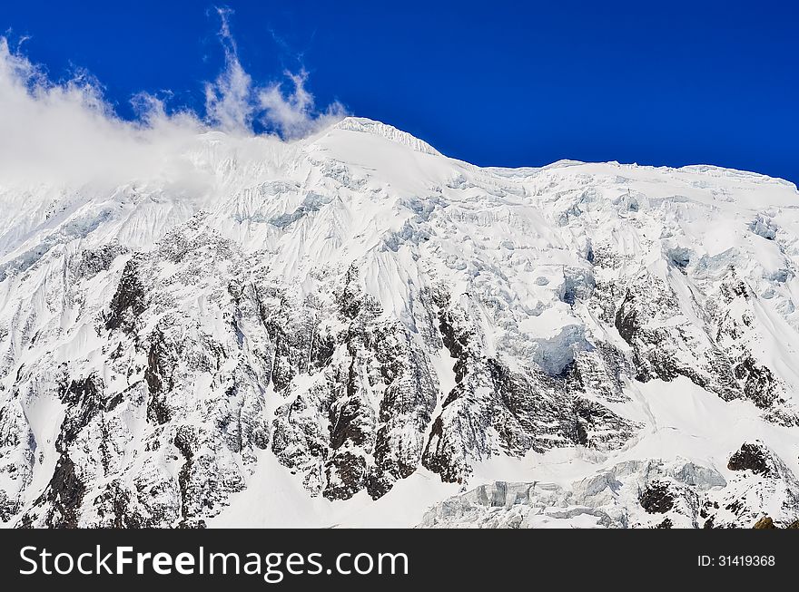 Snow mountain peak with glacier, clouds and blue sky