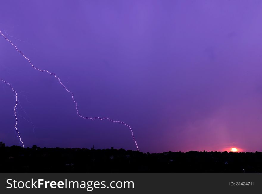 Lightning at sunset on the background of dark blue, purple clouds in the city