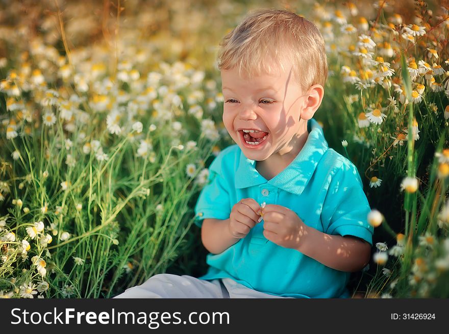 On the nature of the little baby playing and smiling on a field strewn with wild daisies. On the nature of the little baby playing and smiling on a field strewn with wild daisies