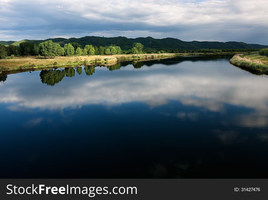 The river channel with a quiet current and clouds reflected in it. The river channel with a quiet current and clouds reflected in it.