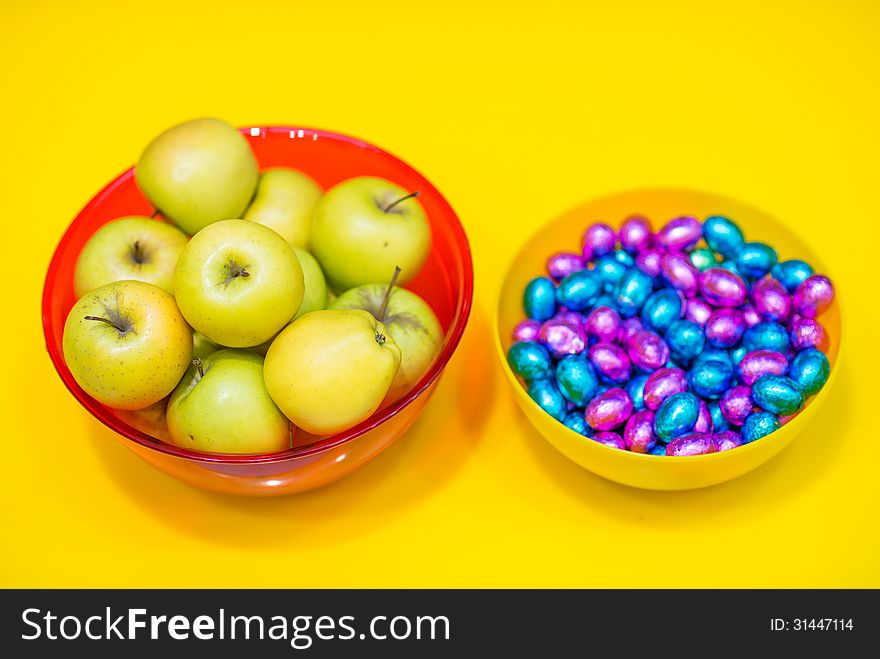 Bowls with green apples and candy on yellow background