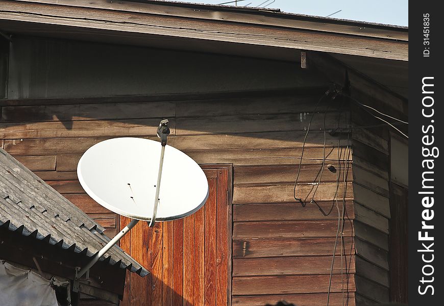 White satellite dish on old wooden house in sunlight. White satellite dish on old wooden house in sunlight