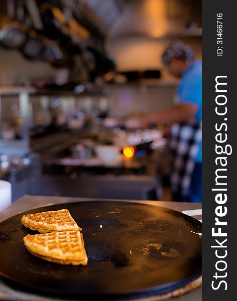Fresh piece of waffles on black plate with blurred cooking chef in background, selective focus