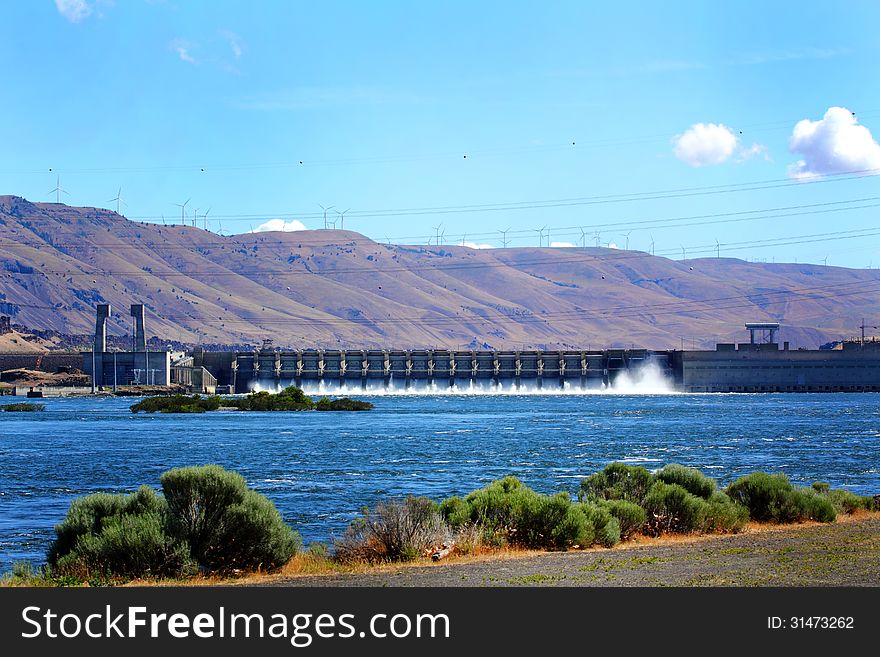 The John Day Dam on the Columbia River with area view of the Washington hills under white fluffy clouds overhead. The John Day Dam on the Columbia River with area view of the Washington hills under white fluffy clouds overhead.