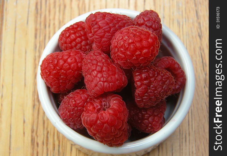 Juicy, ripe, red raspberries are displayed in a white bowl, providing one of the taste sensations of summer.