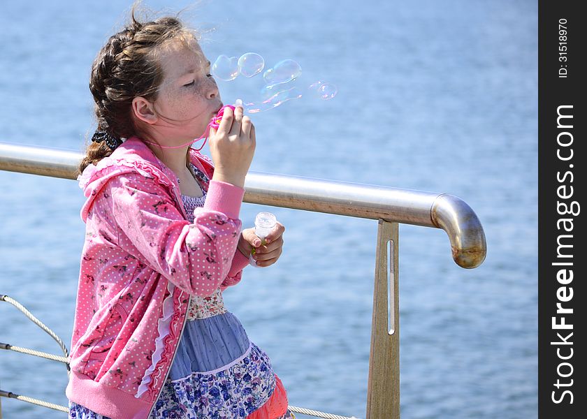 Girl with flecks blowing bubbles on sea background. Girl with flecks blowing bubbles on sea background