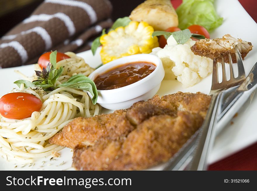 Fried chicken on fork put on dish with pasta and salad. Fried chicken on fork put on dish with pasta and salad