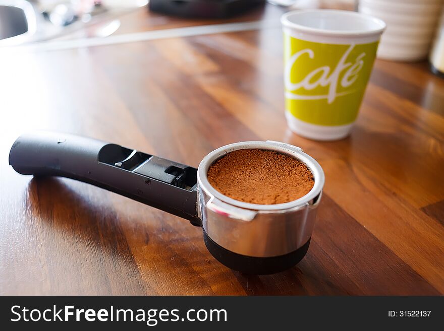 Portafilter with fresh ground coffee on kitchen worktable.