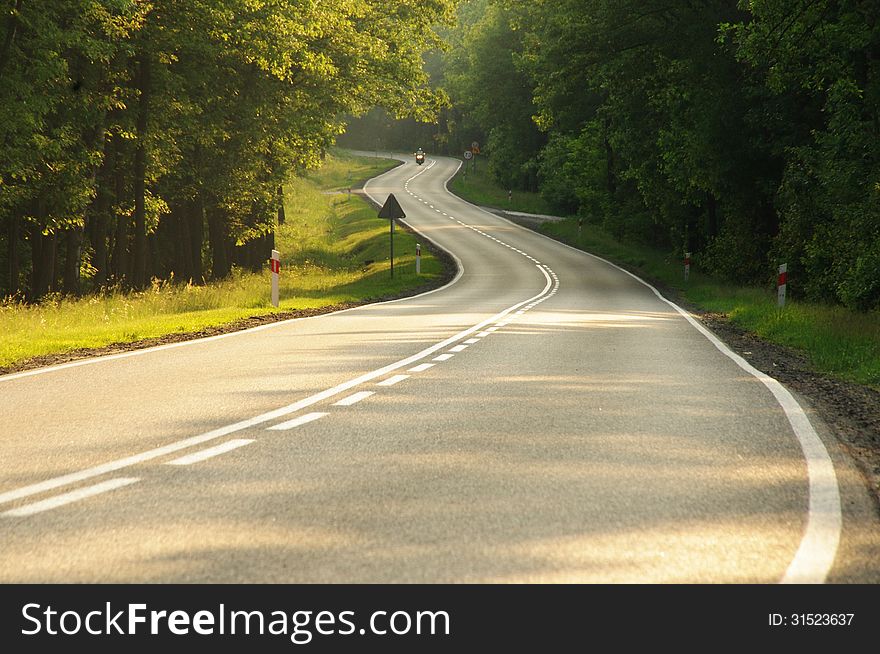 The photograph shows an asphalt road running through the woods. The road climbs the slight rise. The photograph shows an asphalt road running through the woods. The road climbs the slight rise.