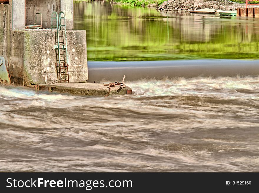 River weir with strong water current and reflections of greenery