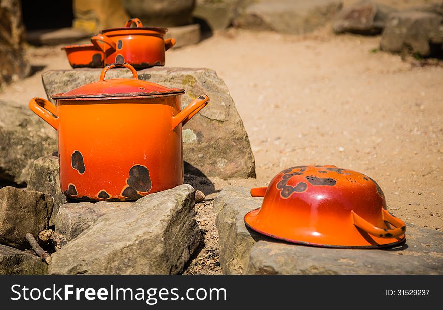 Two old orange pans with lids, together with a old orange bowl and a old orange drainer, drying in the sun ready for use. Two old orange pans with lids, together with a old orange bowl and a old orange drainer, drying in the sun ready for use.