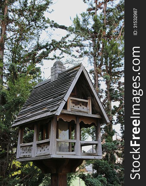 A deluxe wooden birdhouse with tall green pine trees in the background. A deluxe wooden birdhouse with tall green pine trees in the background.