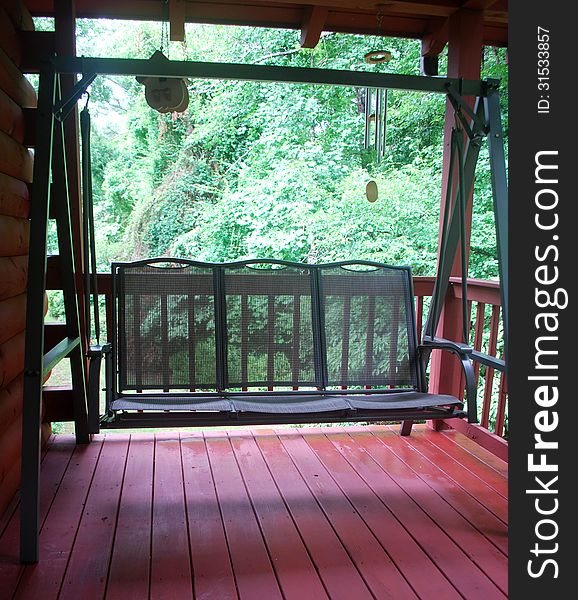 A green porch swing located on the wooden back deck of a log home in the country.