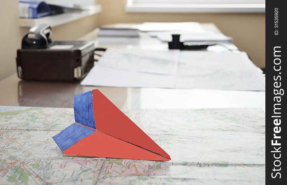 Paper model of an aircraft is on the flight chart. There is a speaking device on the table in the background. Paper model of an aircraft is on the flight chart. There is a speaking device on the table in the background.