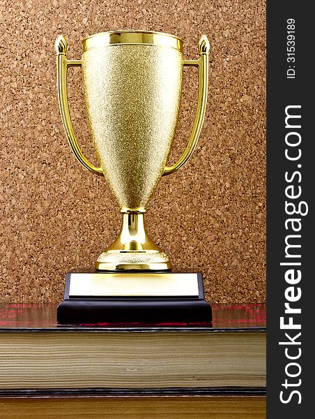 Golden trophy winner cup on stack of books against a cork board. Golden trophy winner cup on stack of books against a cork board.