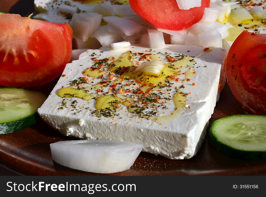 Feta cheese cut in slices, with fresh vegetables, dry herb spices and olive oil - the ingredients for a healthy greek salad. Feta cheese cut in slices, with fresh vegetables, dry herb spices and olive oil - the ingredients for a healthy greek salad