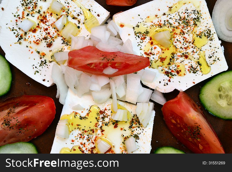 Feta cheese cut in slices, with fresh vegetables, dry herb spices and olive oil - the ingredients for a healthy greek salad. Feta cheese cut in slices, with fresh vegetables, dry herb spices and olive oil - the ingredients for a healthy greek salad