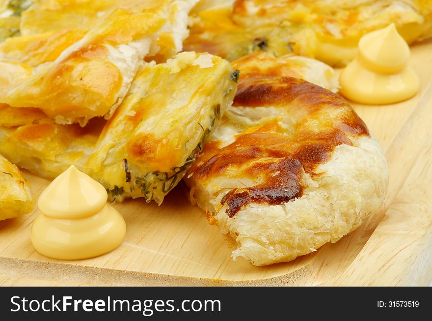 Slices of Cheese and Greens Puff Pastry Pie Garnished with Cheese Sauce closeup on Cutting Board. Slices of Cheese and Greens Puff Pastry Pie Garnished with Cheese Sauce closeup on Cutting Board